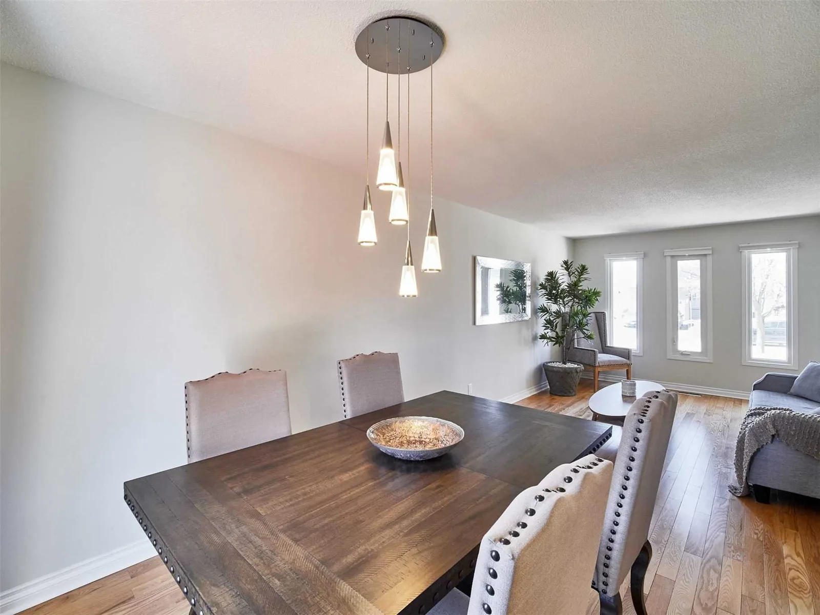 Dining room with a cone pendant light, dark wood table and upholstered chairs, open to the living room