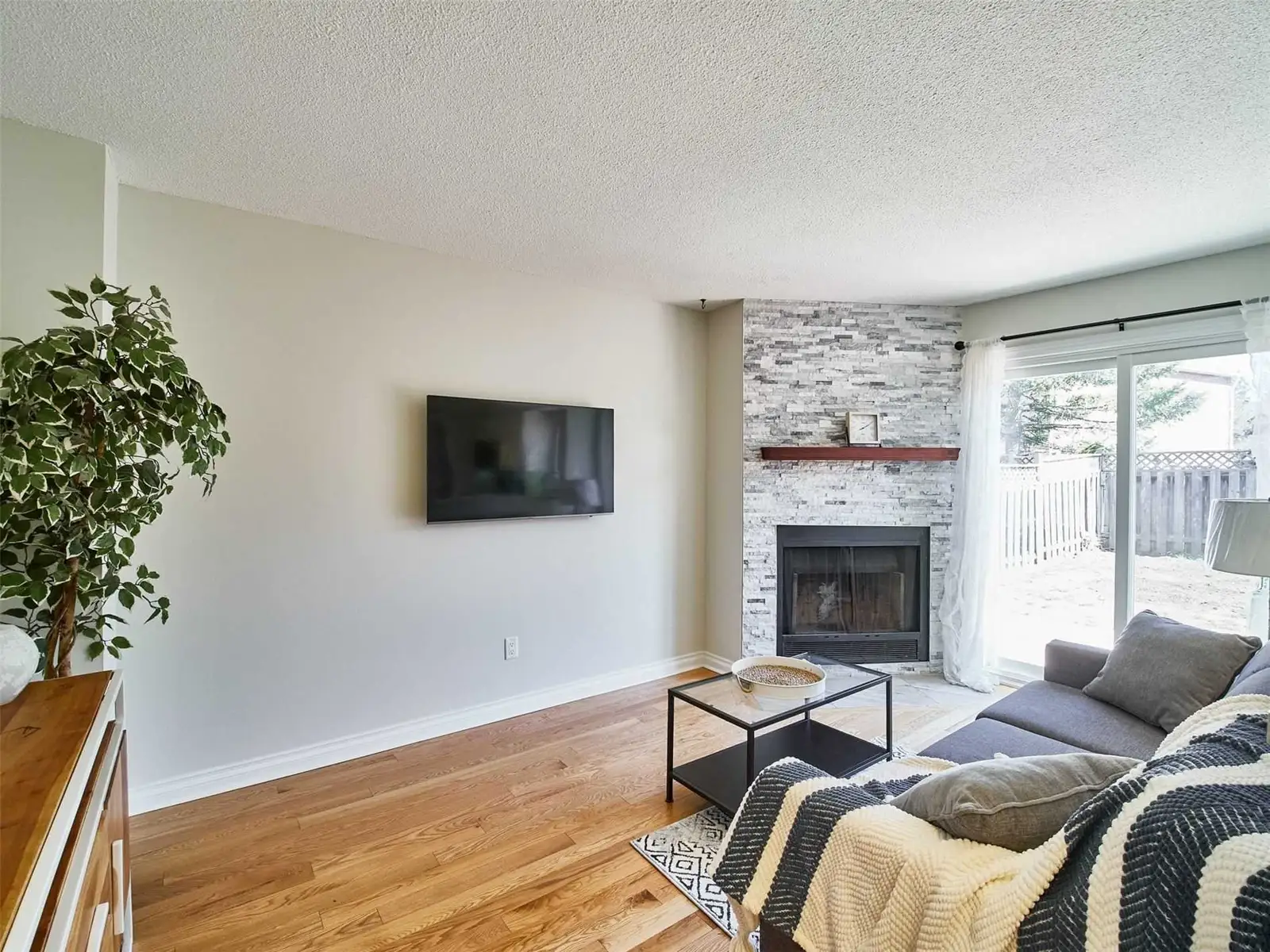 Family room with a stone-surround fireplace, hardwood floors and a sliding door to a fenced backyard