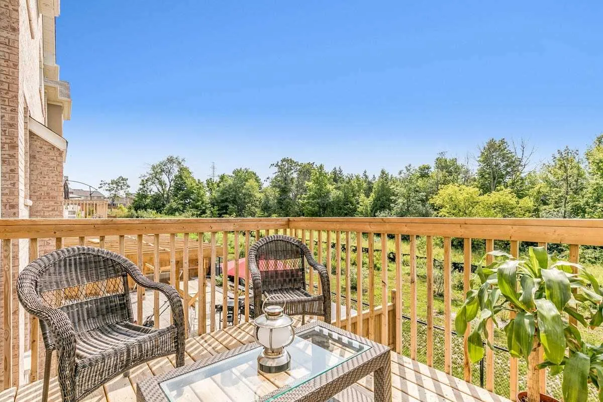Wooden deck with two wicker chairs and a glass-top table overlooking a green ravine