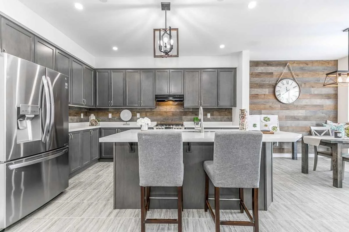 Kitchen with grey shaker cabinets, white quartz island with two bar stools, stainless steel fridge and a barn-board feature wall