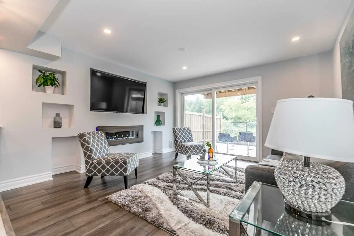 Living room with light grey walls, built-in niches, a linear fireplace, wood-look floors and a sliding door to the backyard